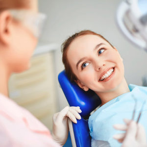 Girl sitting in a dental chair with a beautiful smile talking to hygienist